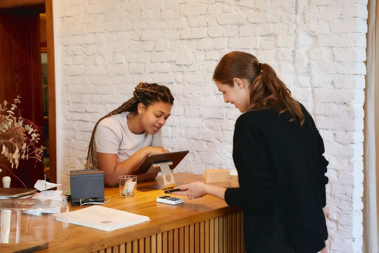 Two women talking at a reception desk with a tablet.