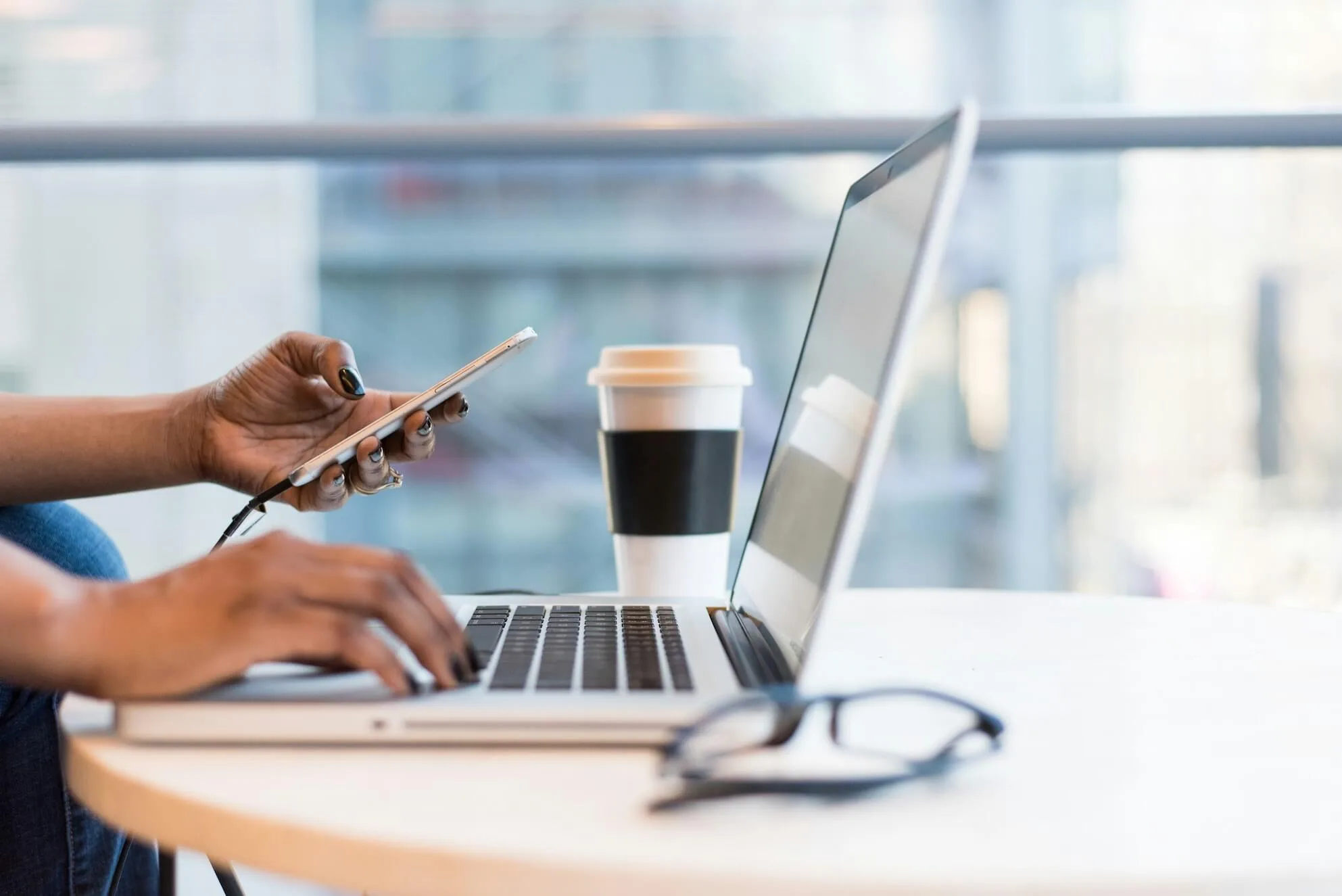 A person using a smartphone and typing on a laptop.