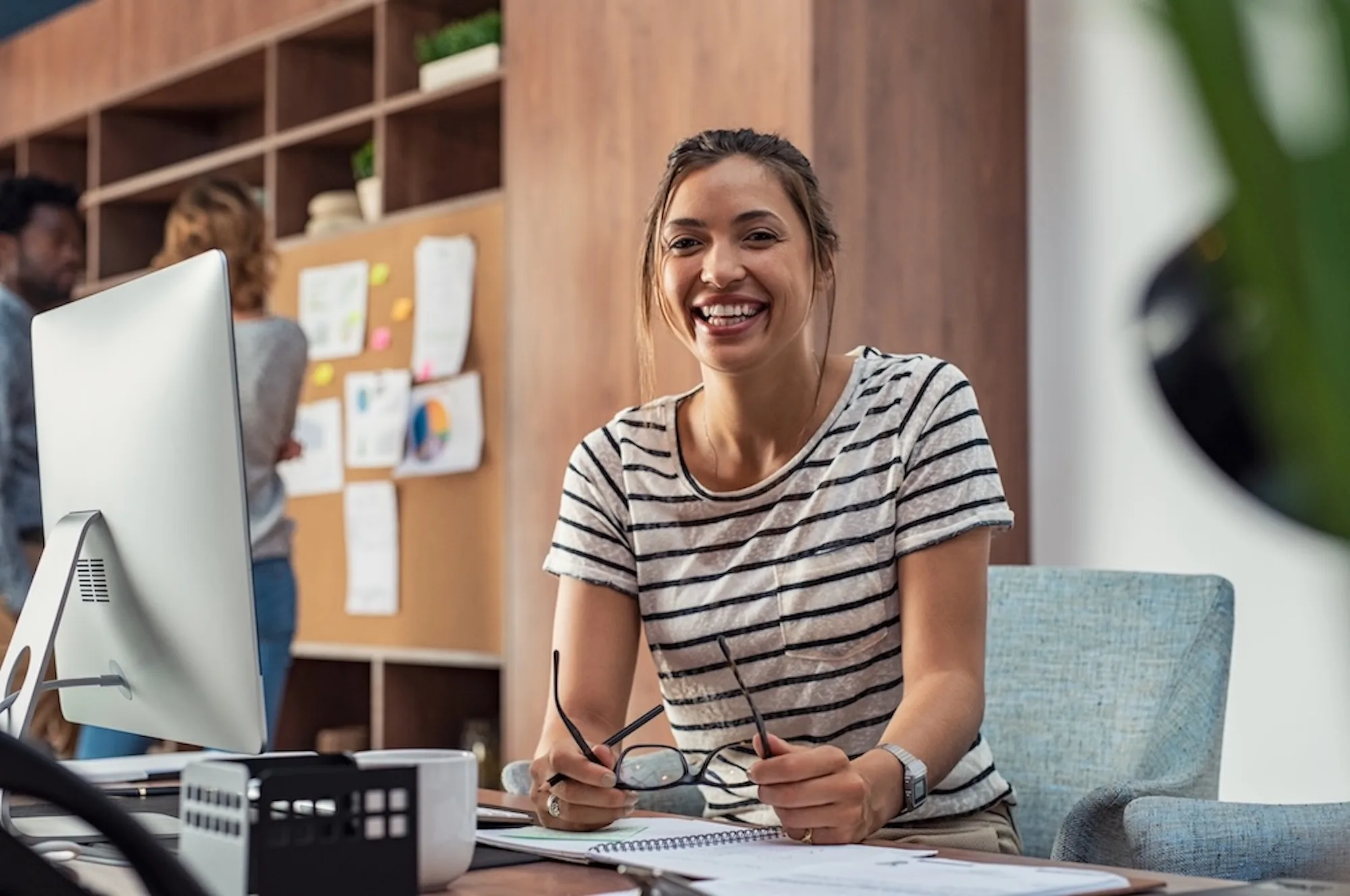 A woman smiling at her desk in an office setting.