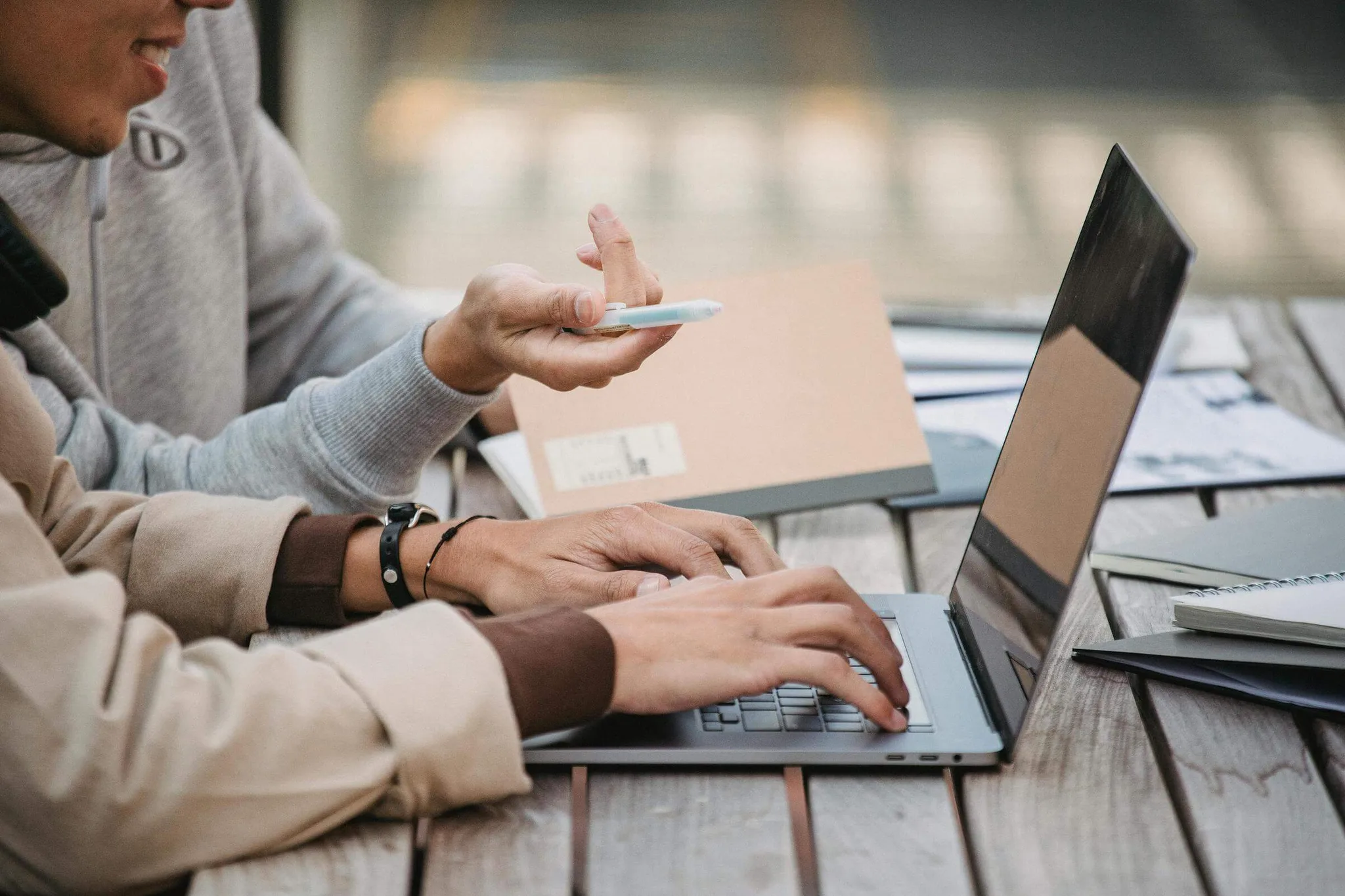 Two people collaborating over a laptop at a wooden table.