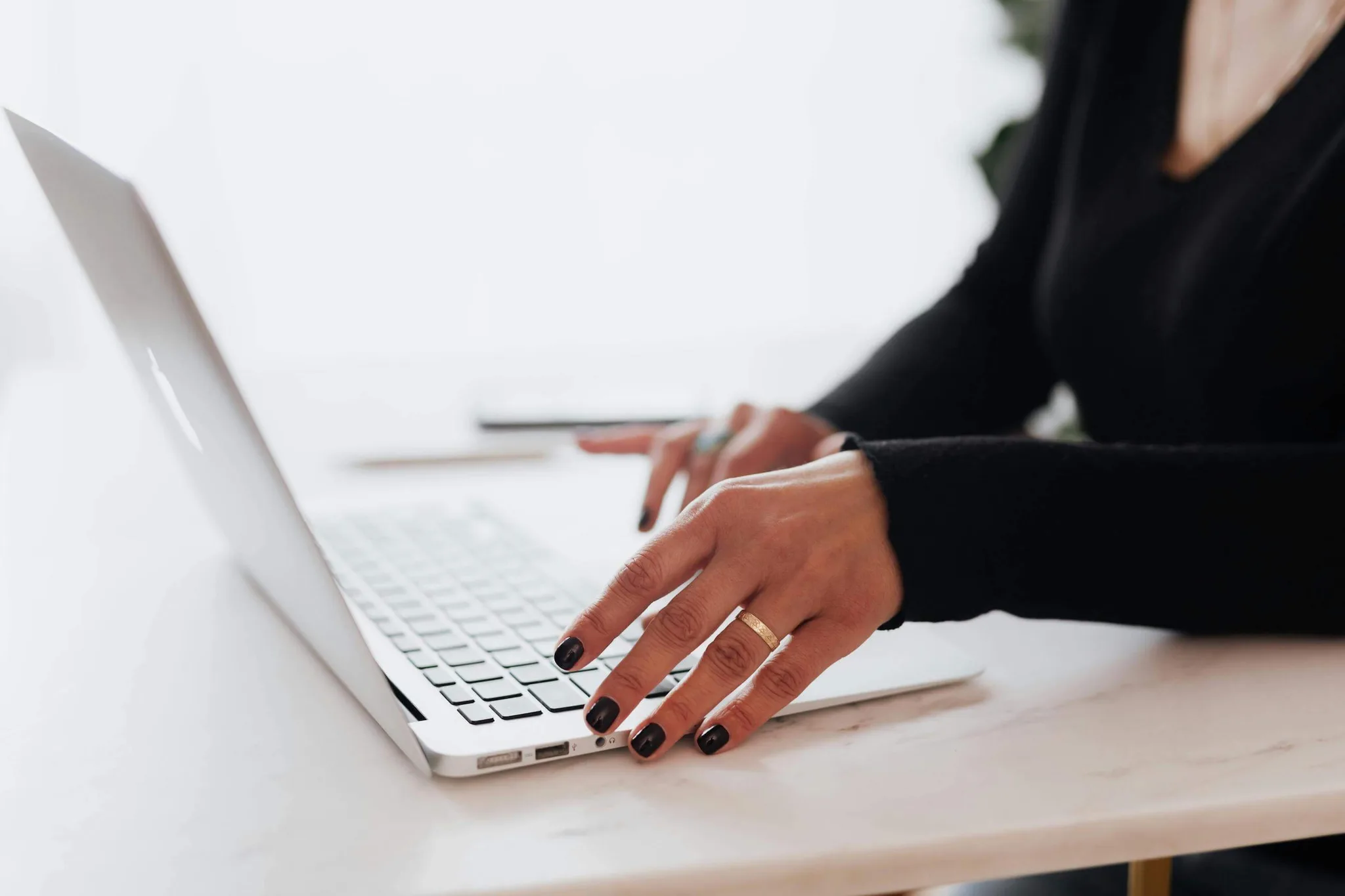 A person typing on a silver laptop at a white table.