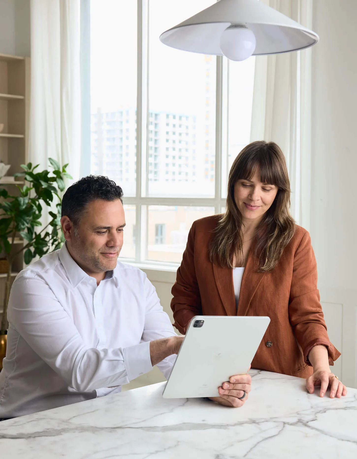 Two people collaborating at a marble table with a tablet.
