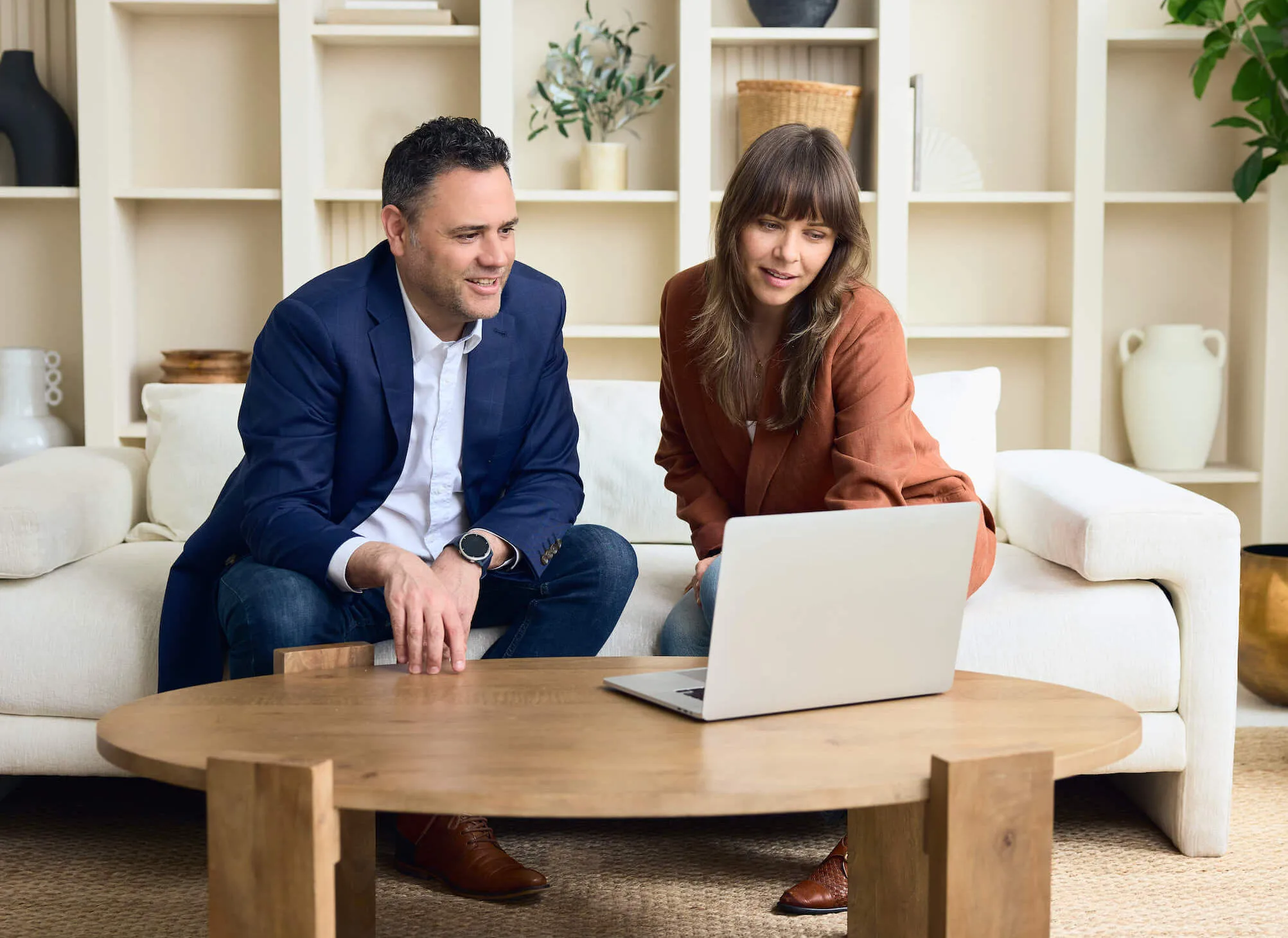 Two adults working together on a laptop in a living room.