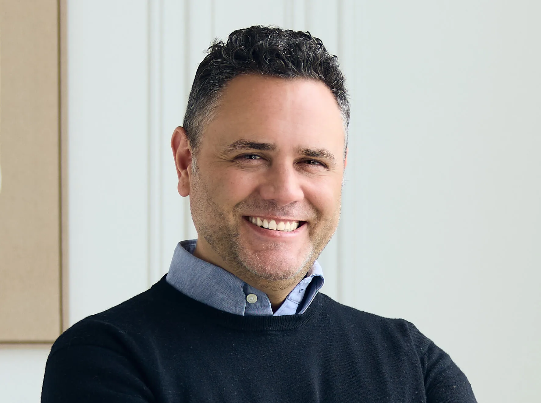 A smiling man in a dark sweater with curly hair.