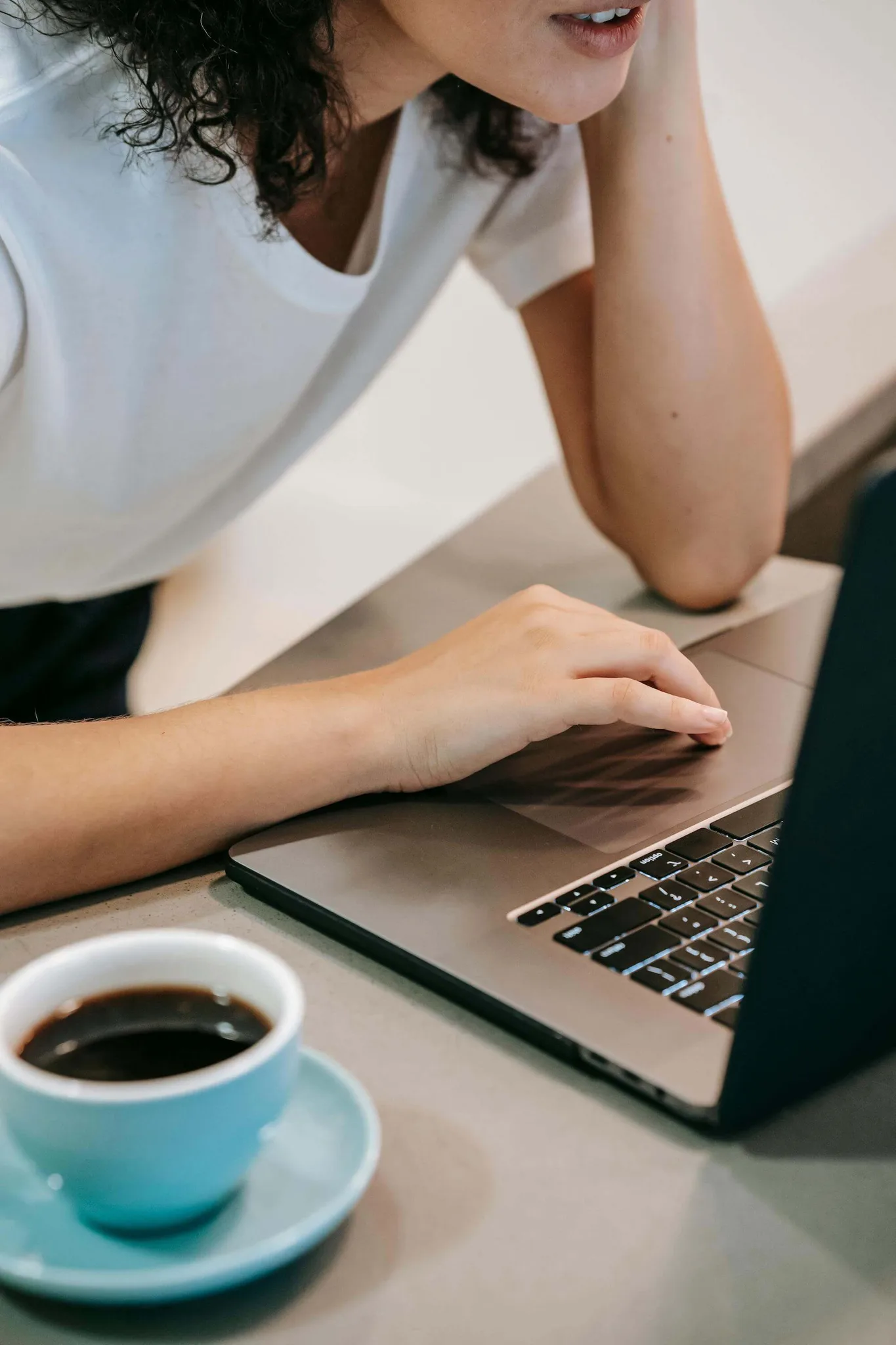 A woman working on a laptop with coffee beside her.