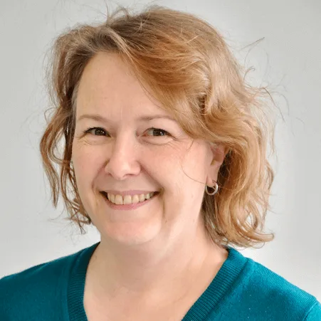 Smiling woman with curly hair wearing a teal sweater.