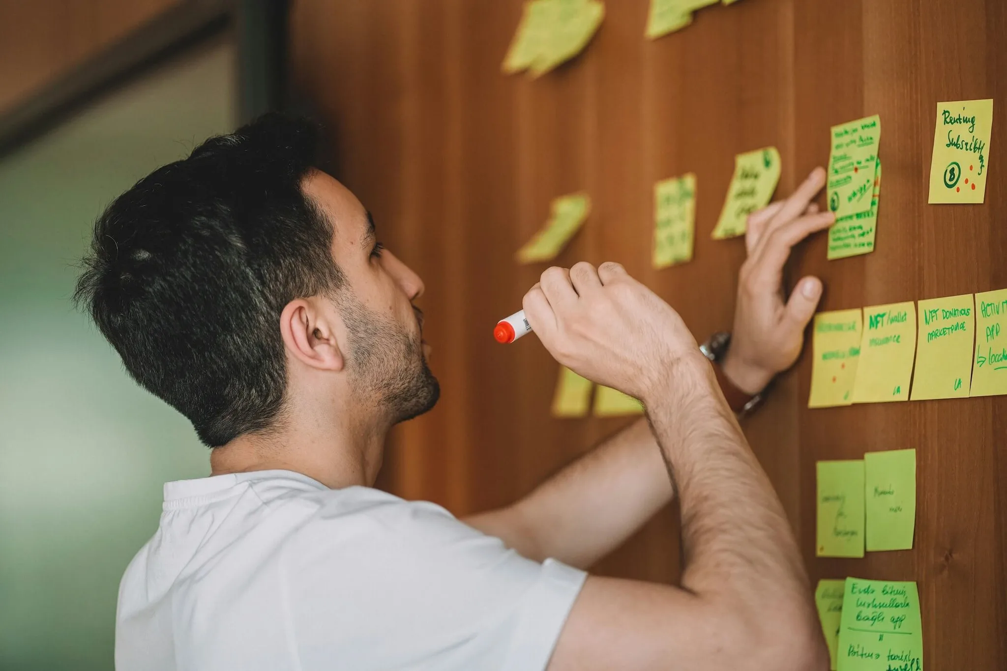 A man writing on a sticky note on a wooden wall.
