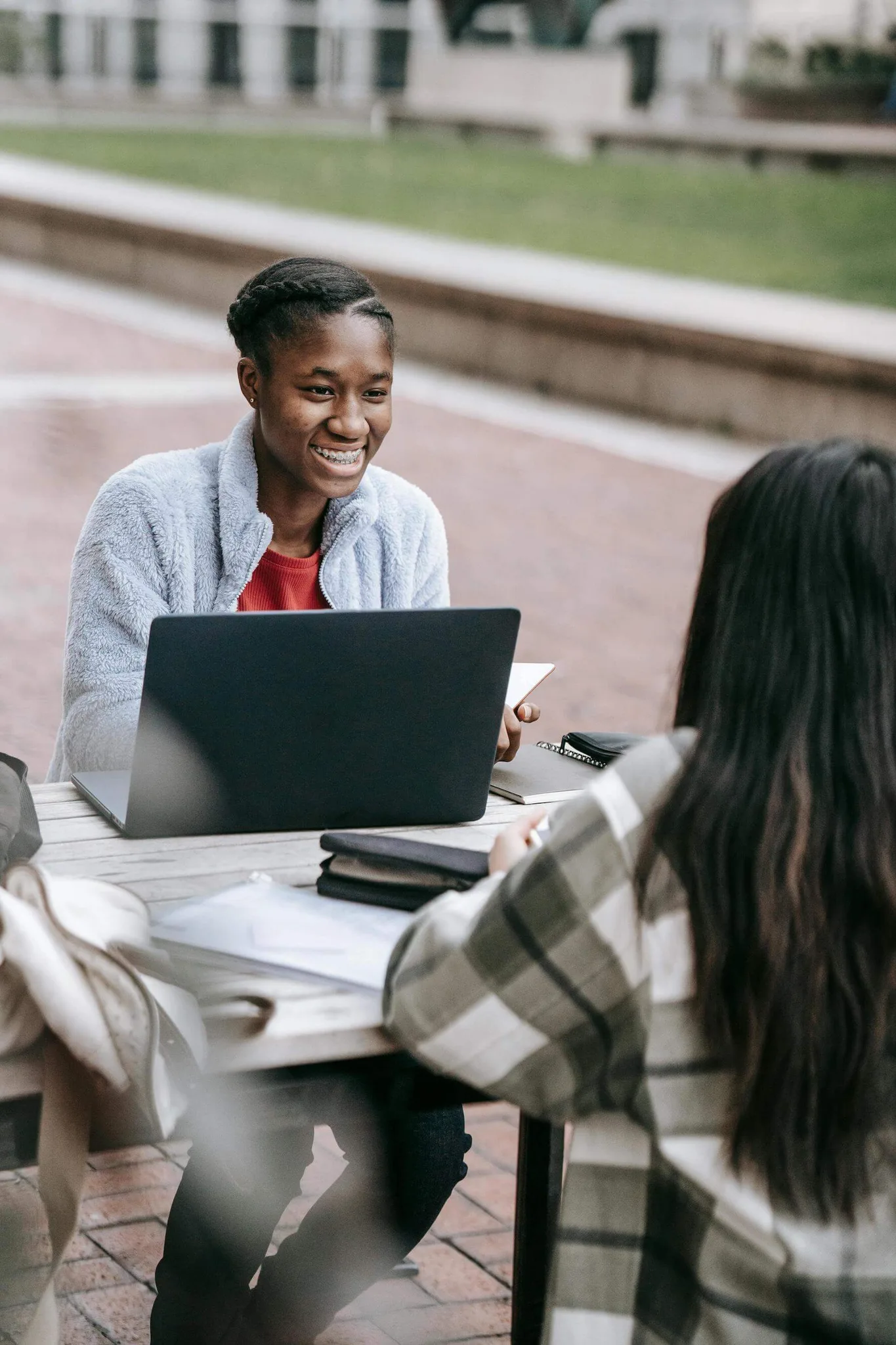 Two women discussing with a laptop at an outdoor table.