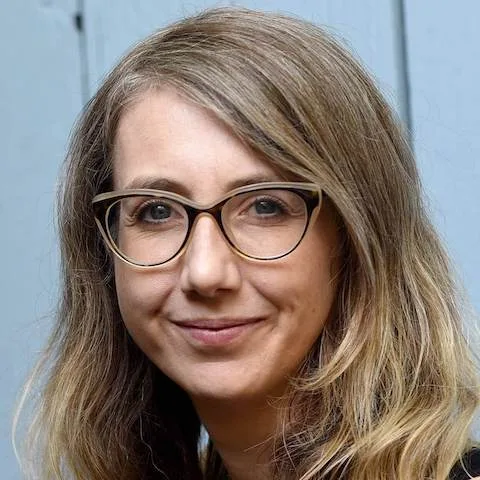 A smiling woman with glasses in front of a blue background.