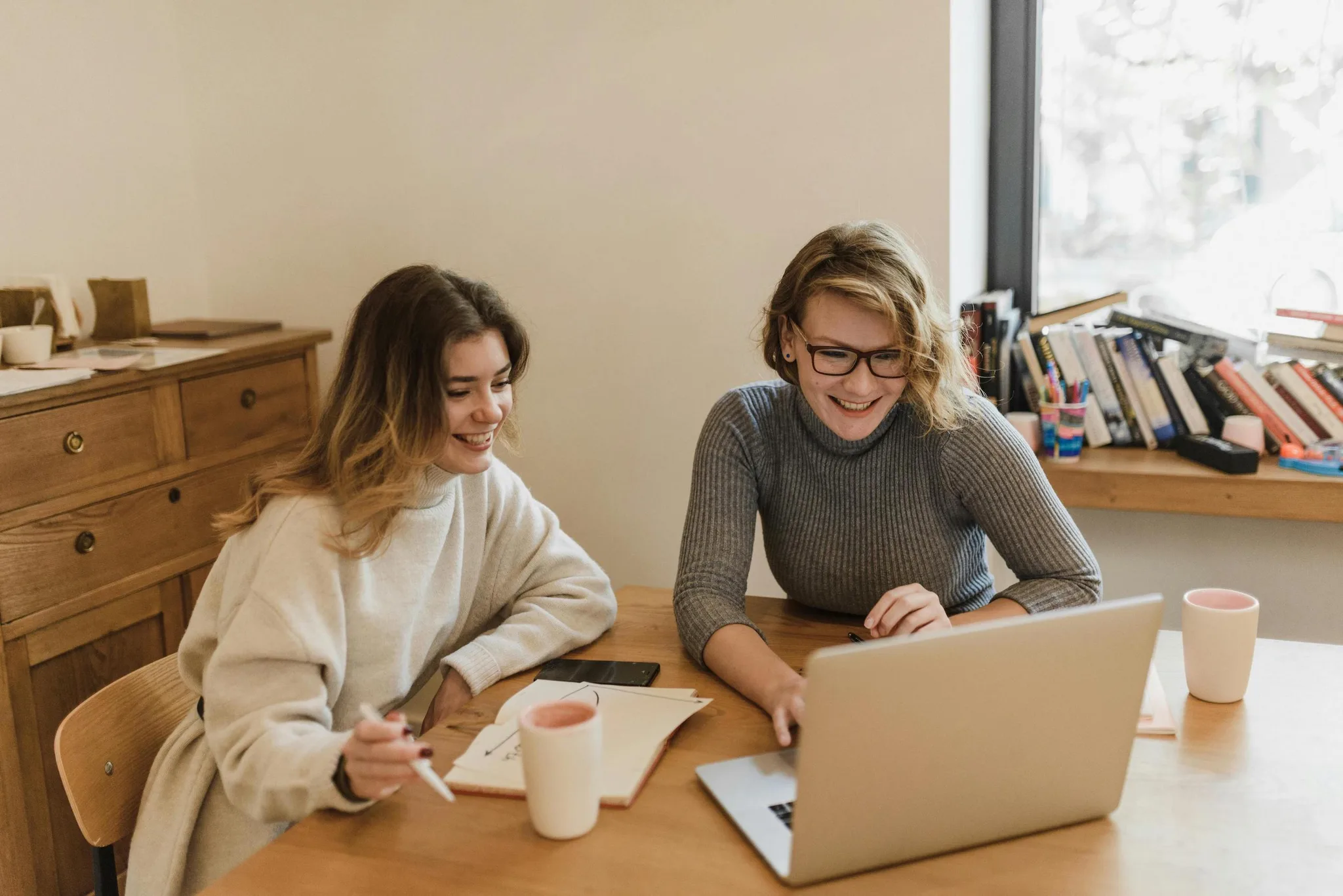 Two women collaborating on a laptop at a wooden table.