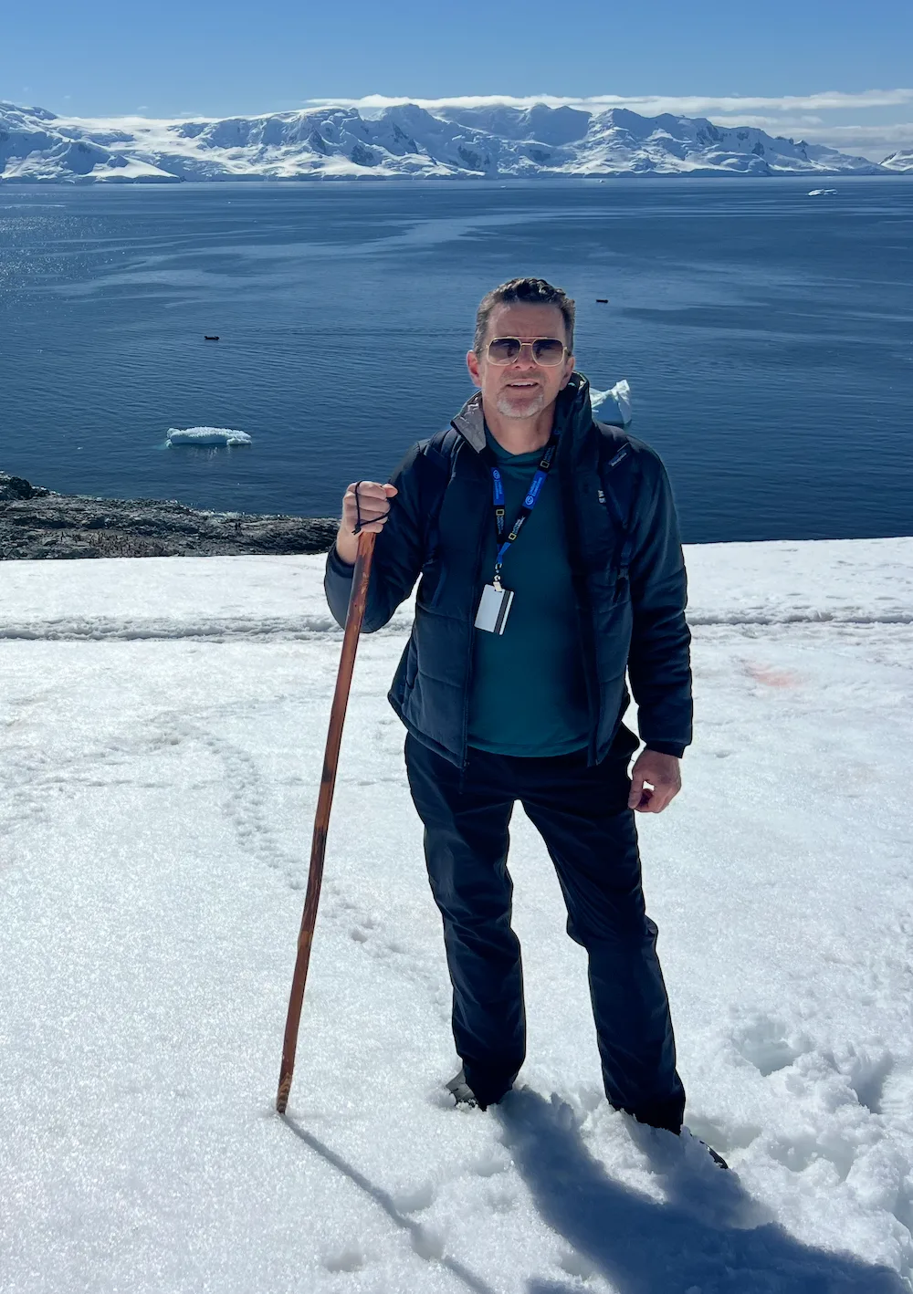 A person on snow with mountains and water in the background.