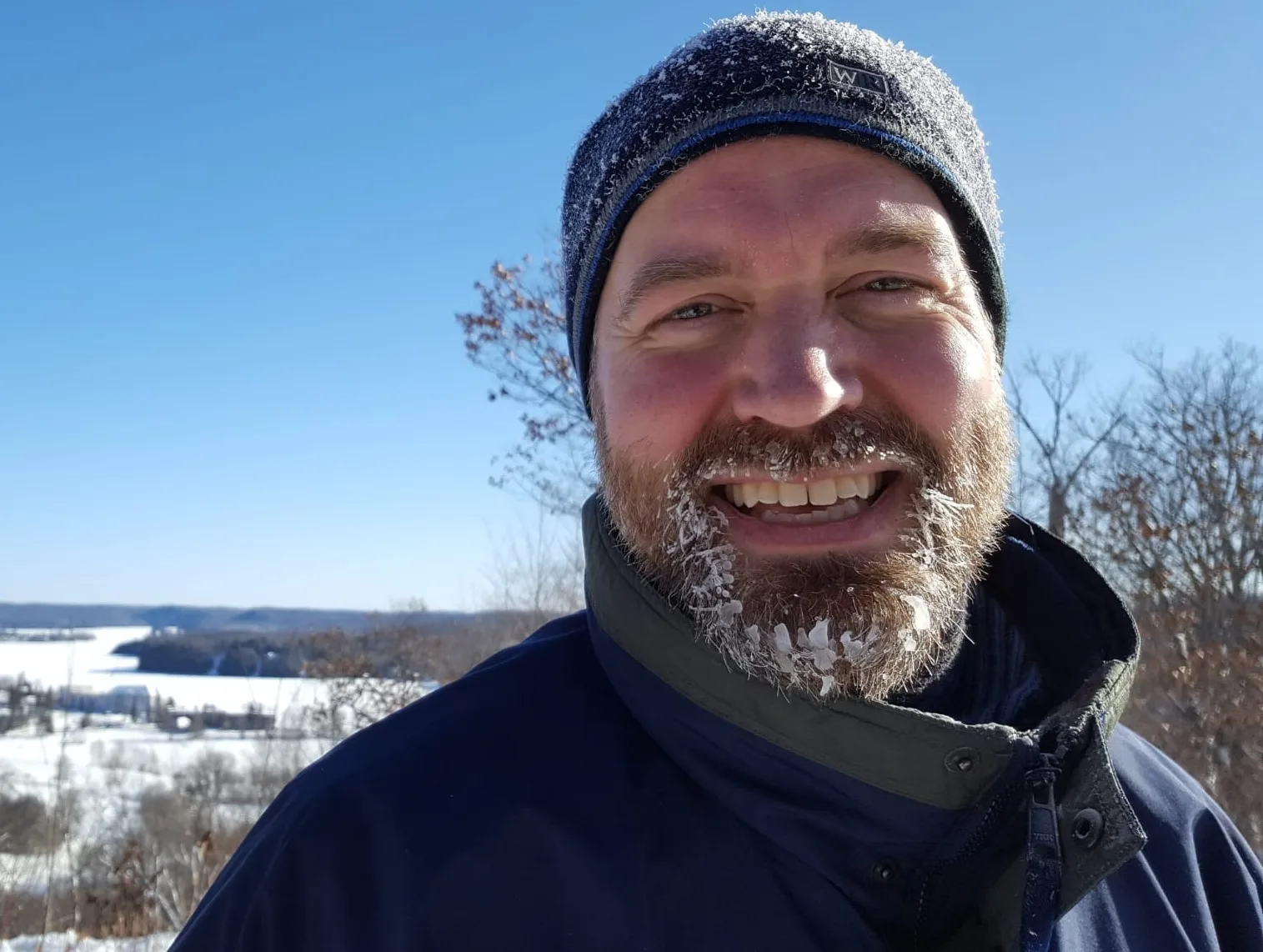 A man with a frosty beard smiles in a snowy landscape.