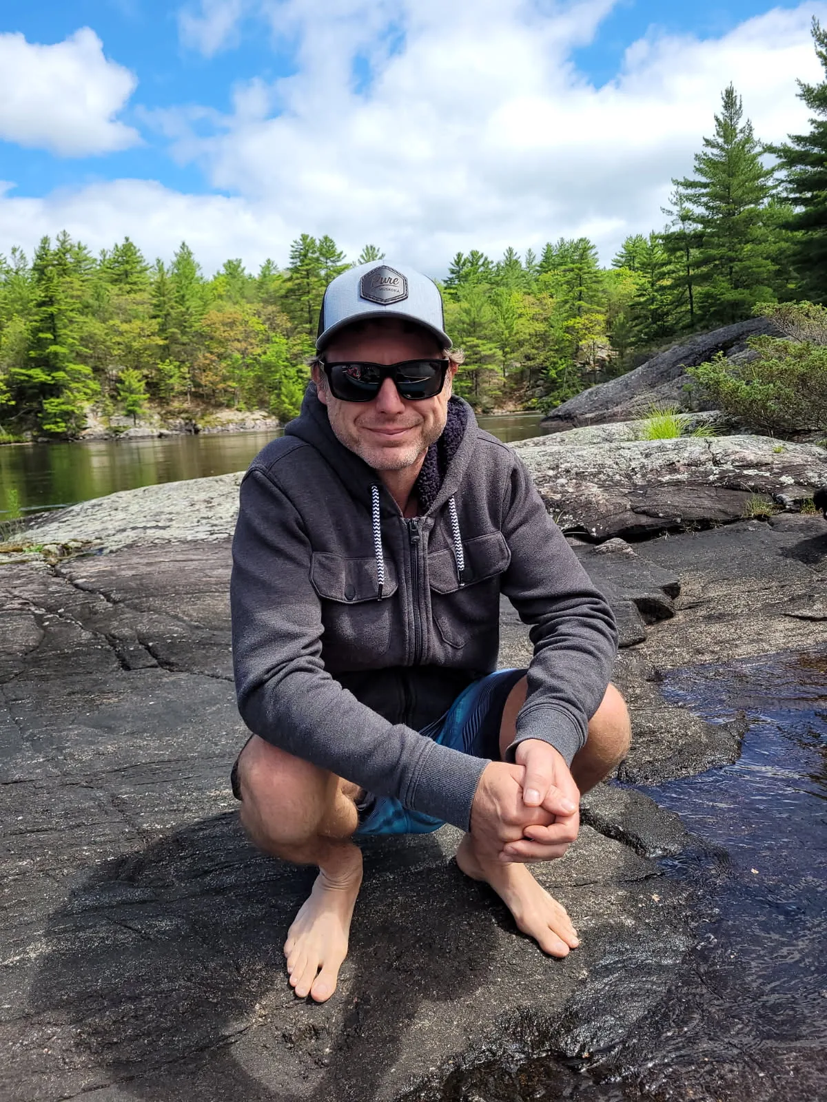 A man squatting on rocks by a river.