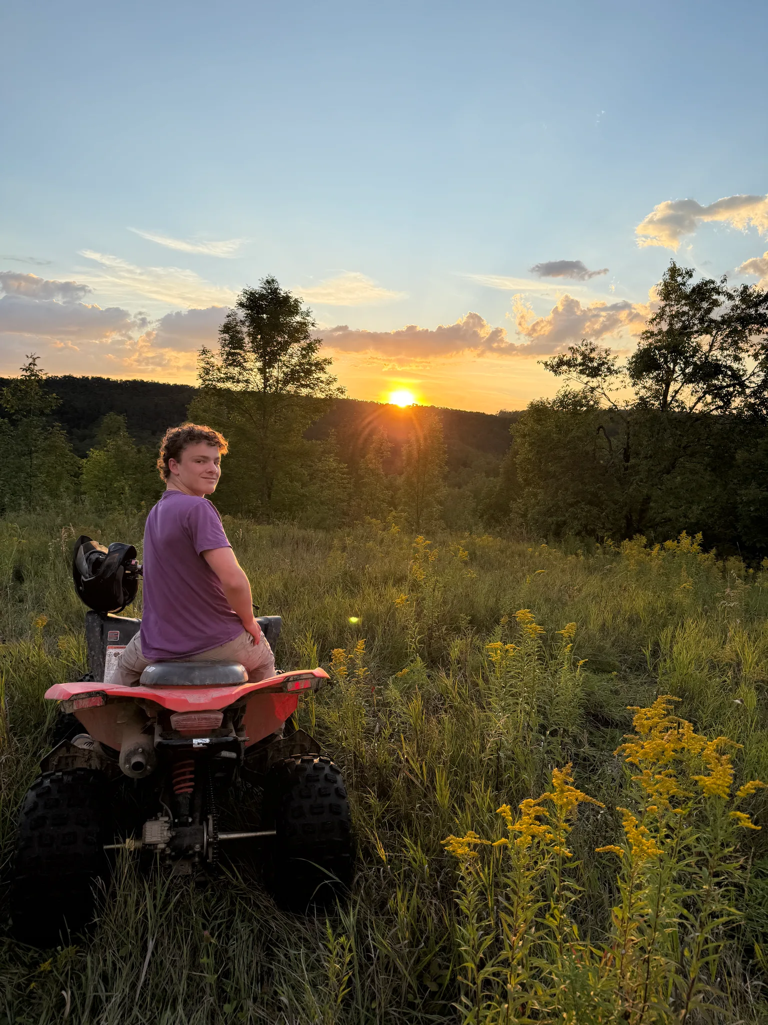 A person on an ATV watching the sunset in a field.