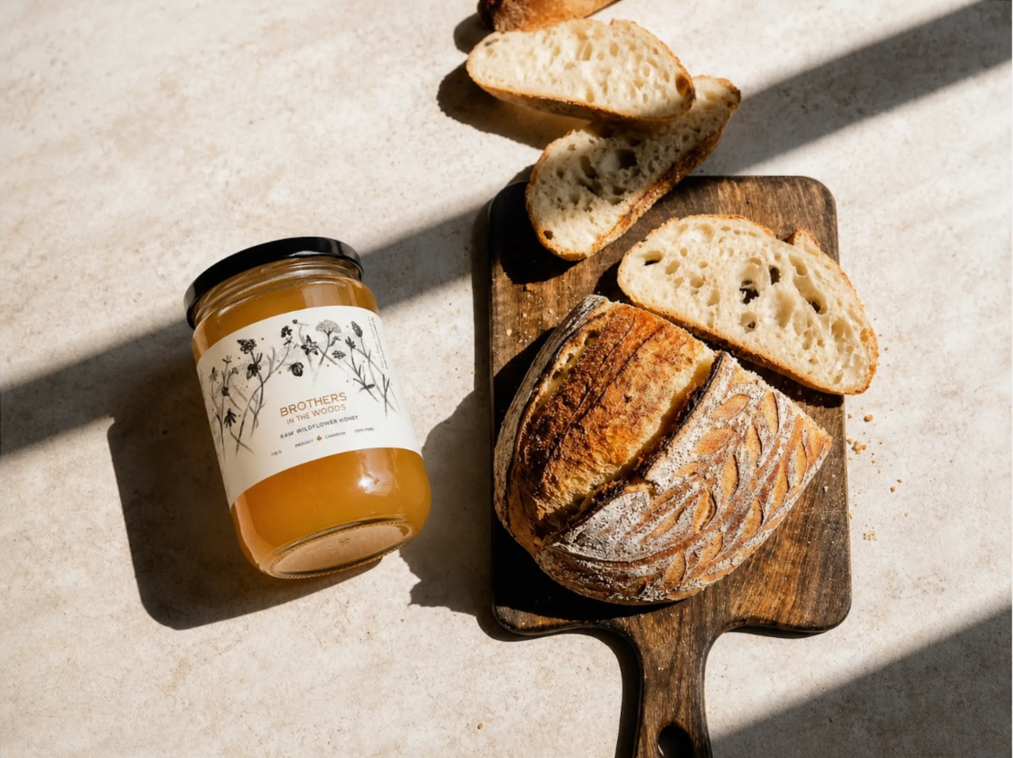 A jar of honey next to a loaf of bread on a cutting board.