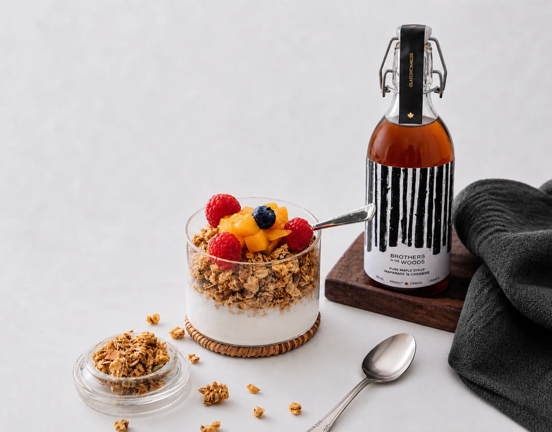 Yogurt parfait with granola and maple syrup bottle.