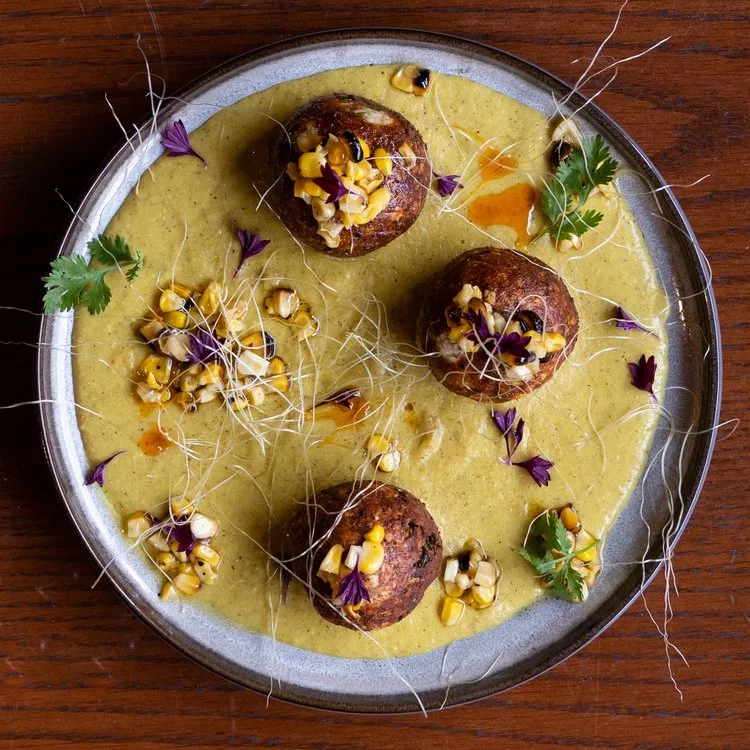 A plate of golgappas with yellow sauce and garnishes.