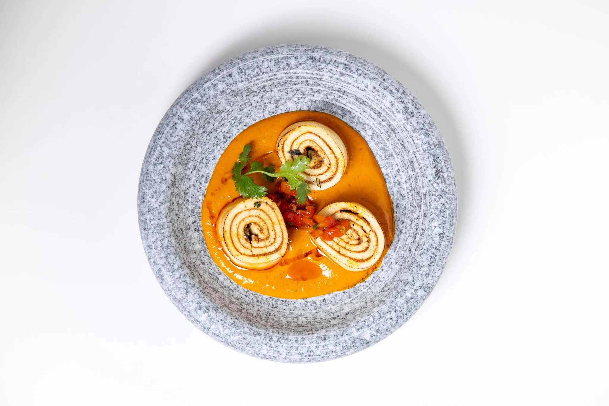 Rolled Indian flatbread in orange sauce on a gray plate.