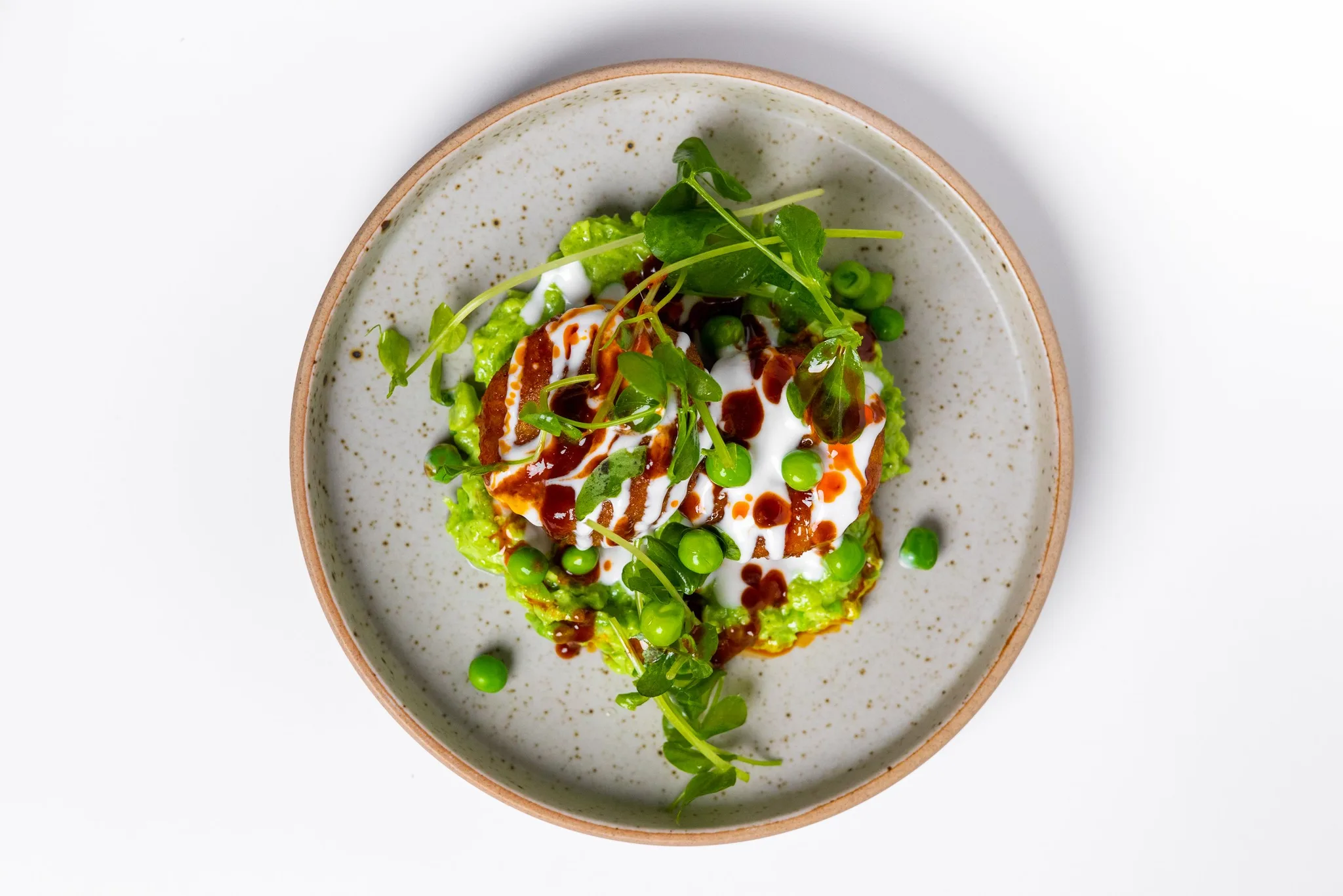A colorful pea dish with yogurt and herbs on a plate.