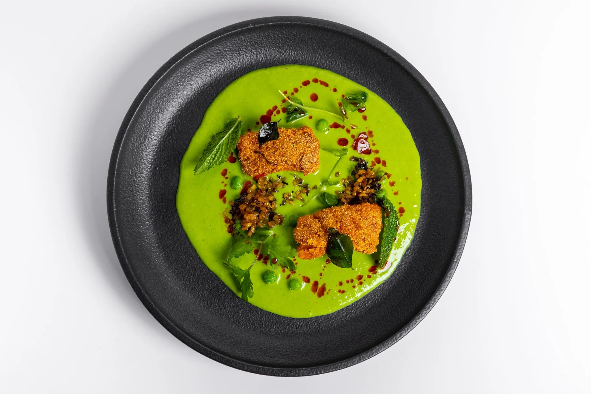 A vibrant dish of green pea puree and fritters on a dark plate.