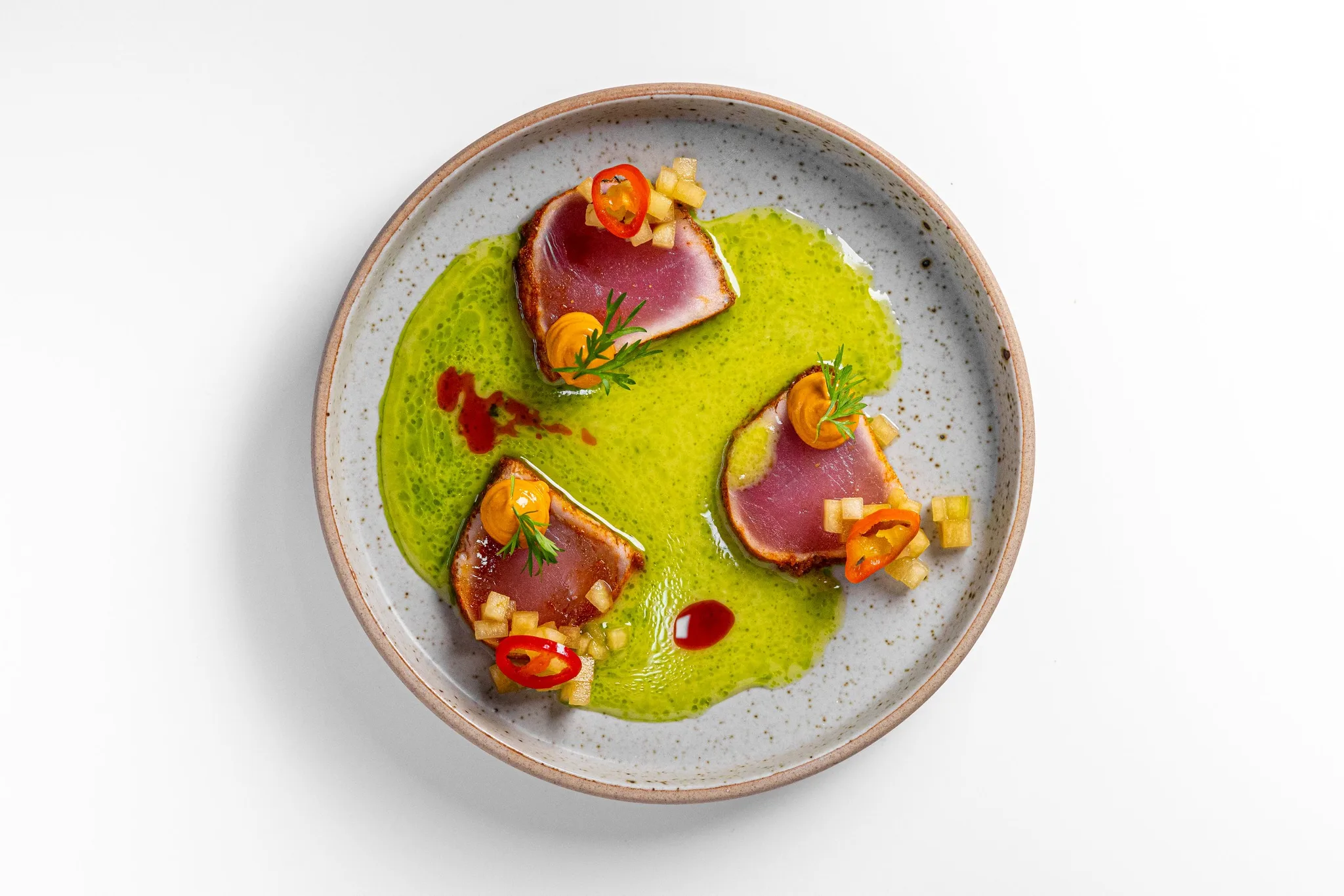 Seared tuna slices on a plate with colorful garnishes.