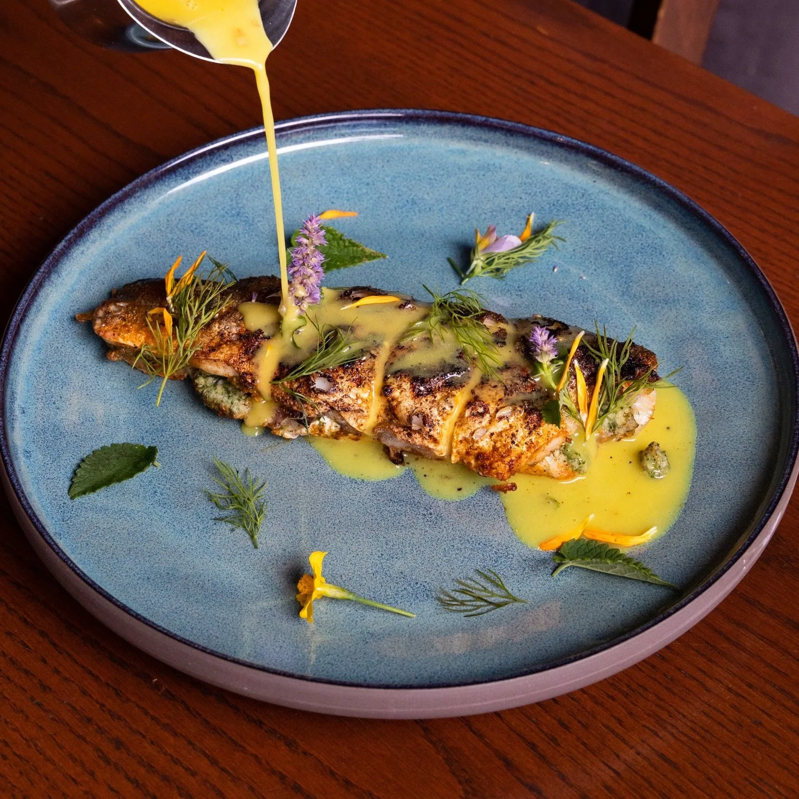 Grilled fish fillet with herbs and yellow sauce on a blue plate