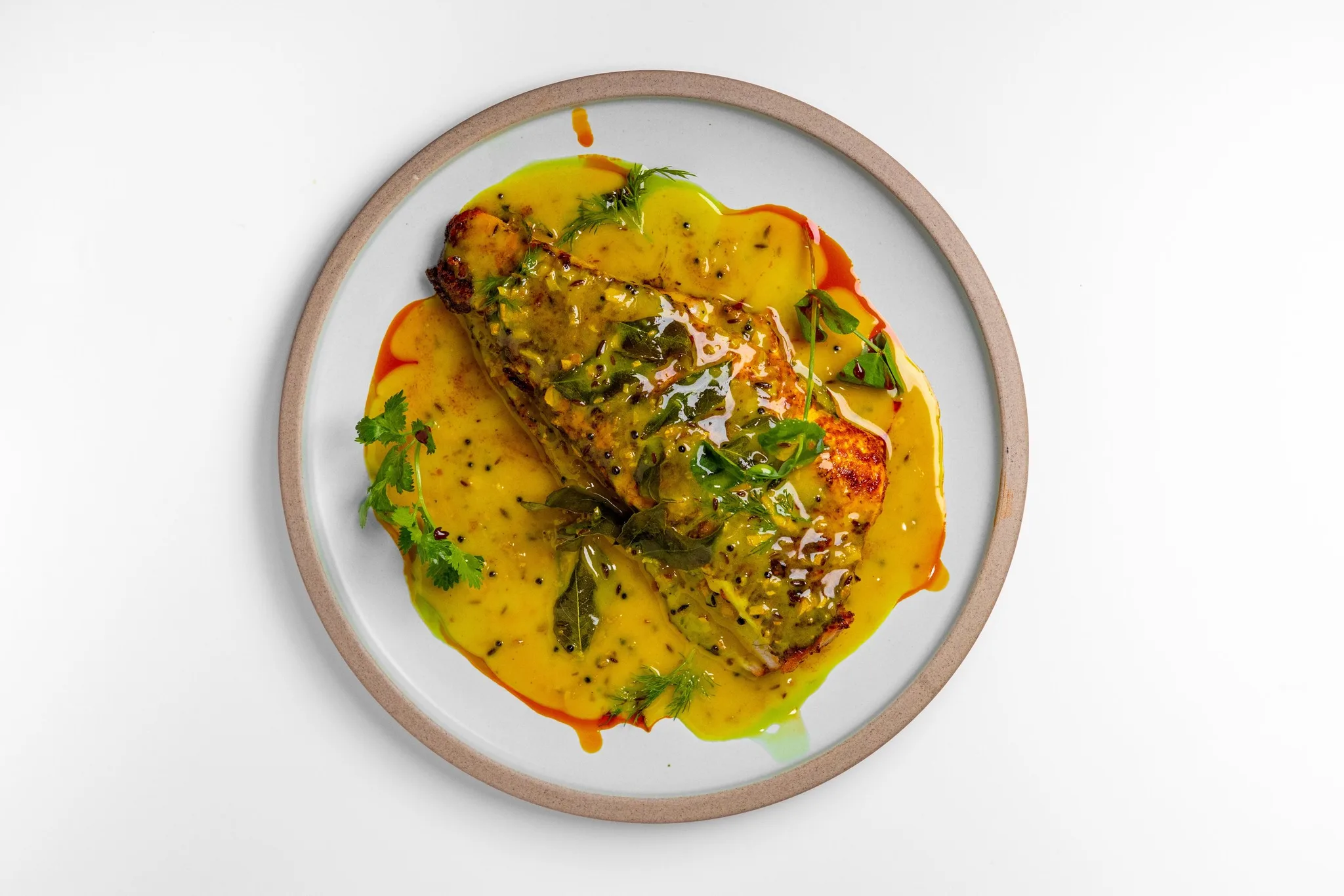 Grilled fish fillet with yellow sauce and herbs on a plate.