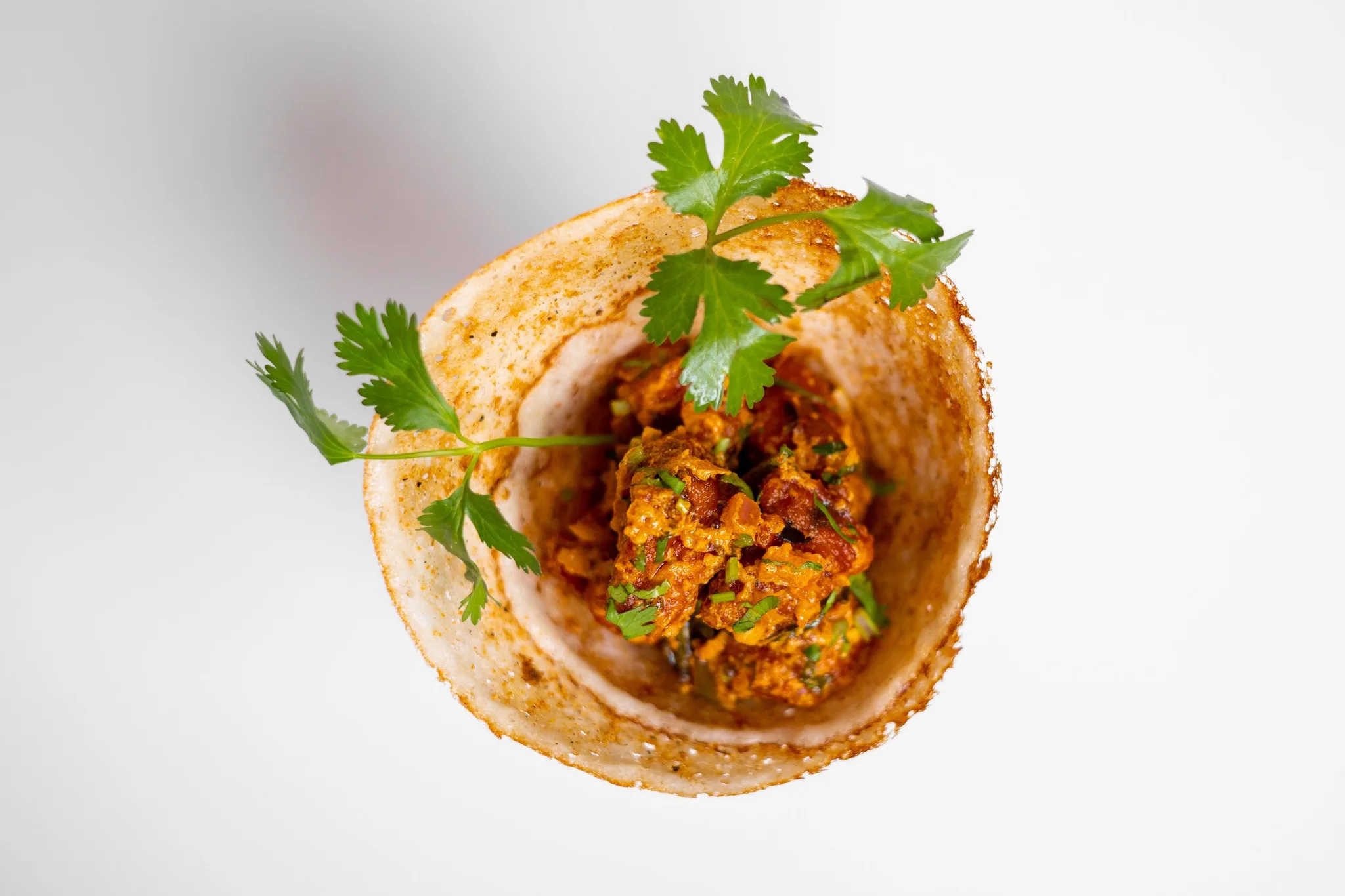 A dosa cone filled with spiced vegetables and cilantro.
