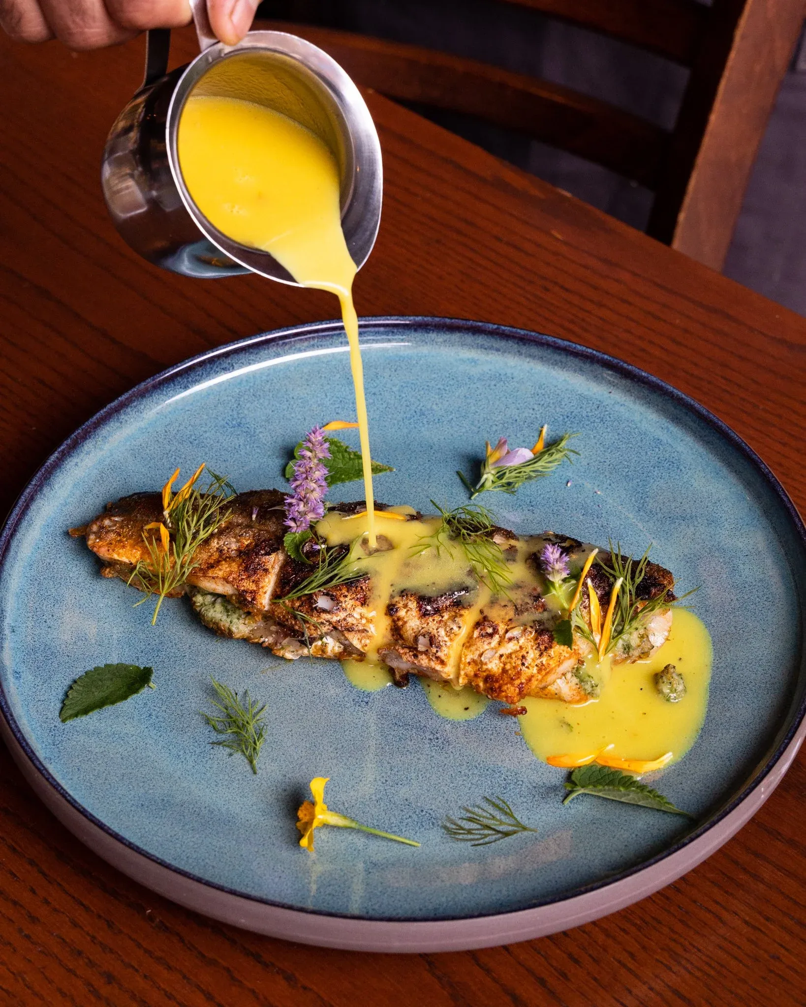 A piece of fish with yellow sauce garnished with herbs and flowers.