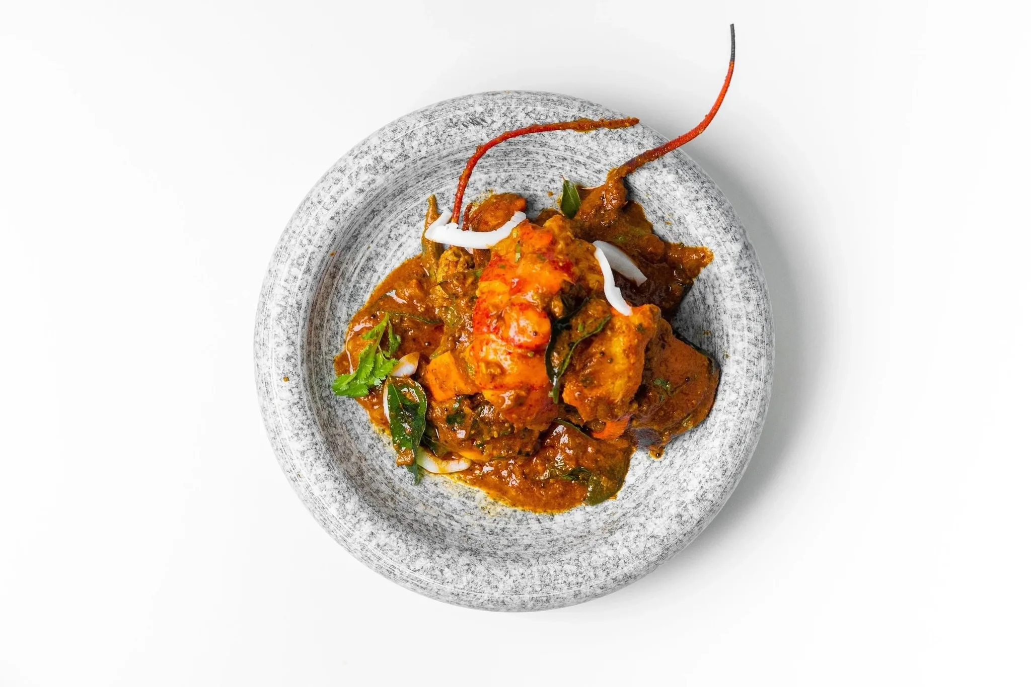 A plate of chicken curry with herbs and chili.