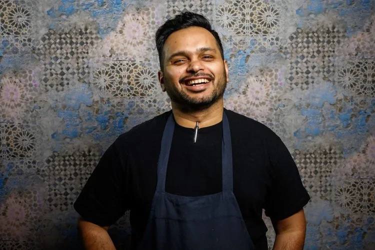 A smiling chef in front of a decorative background.