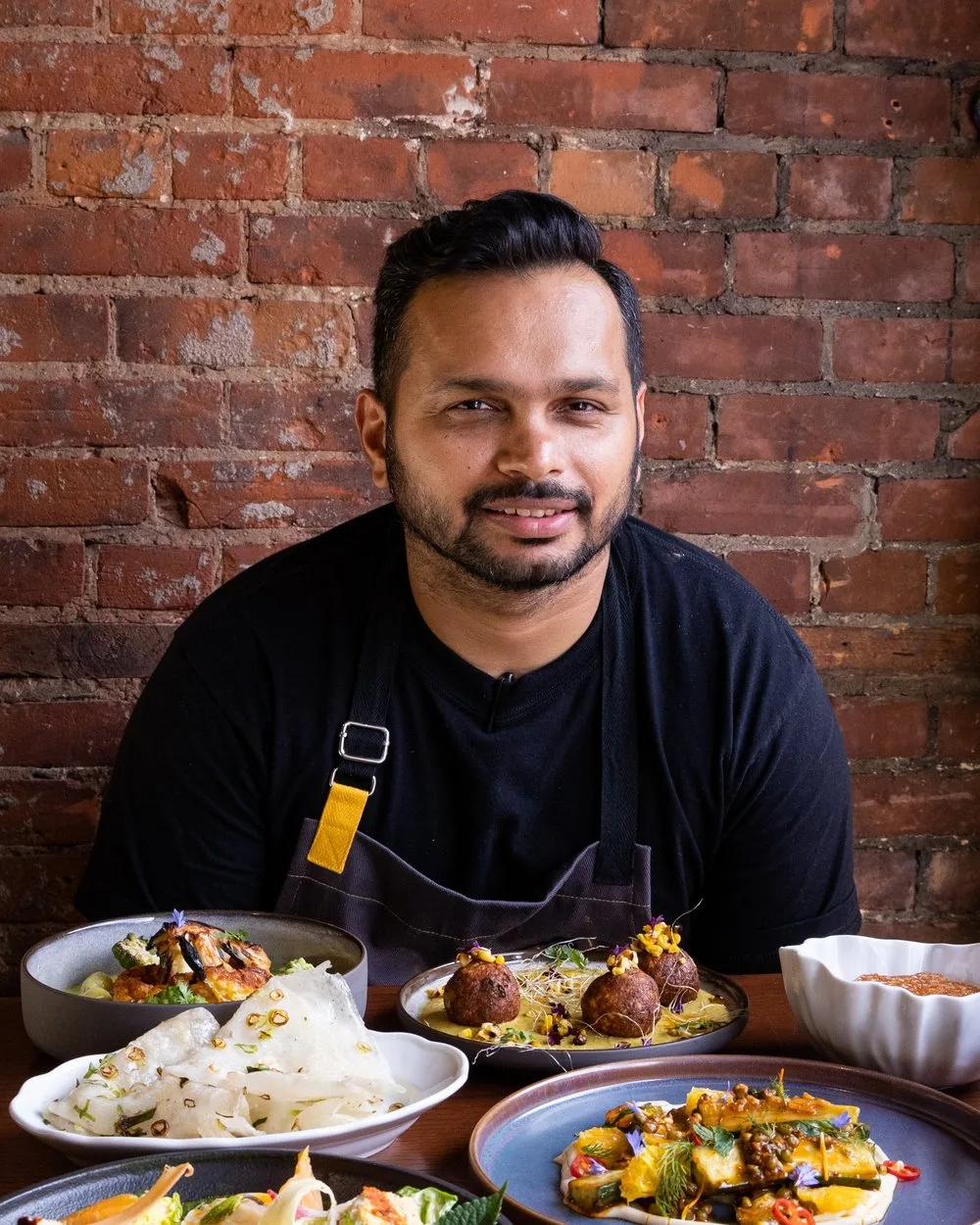 Chef smiling with Indian dishes in front of him.