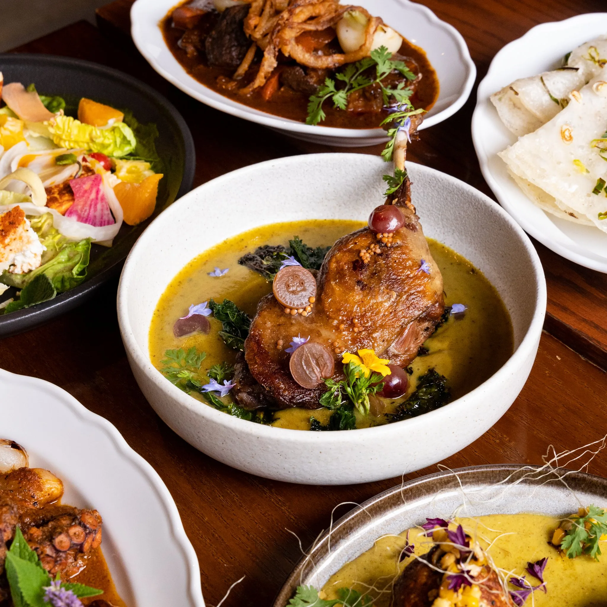 A dish of slow-cooked duck in curry sauce with garnishes.
