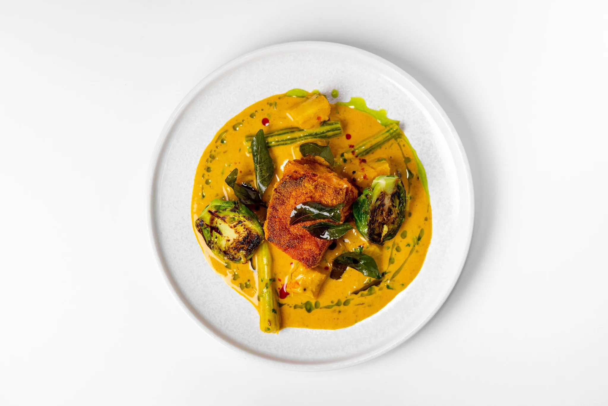 A plate of vibrant Indian curry with seared protein and vegetables.