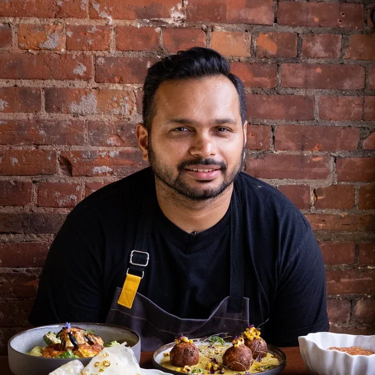 A chef with Indian dishes in front of a brick wall.
