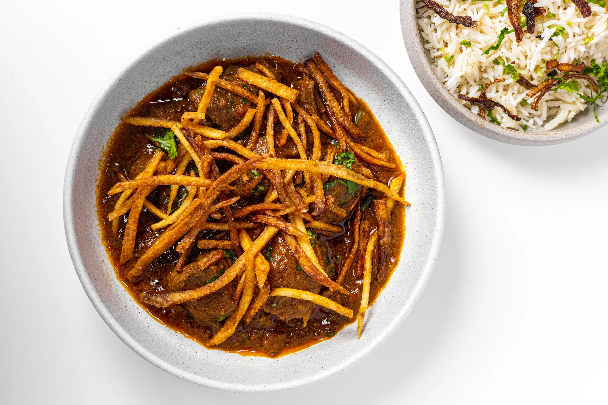 A bowl of curry with fried noodles and rice on the side.