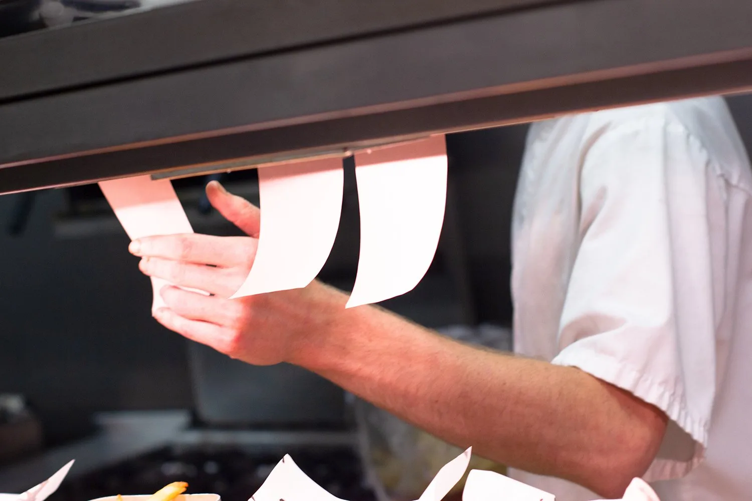Chef's hand holding order tickets in a busy kitchen.
