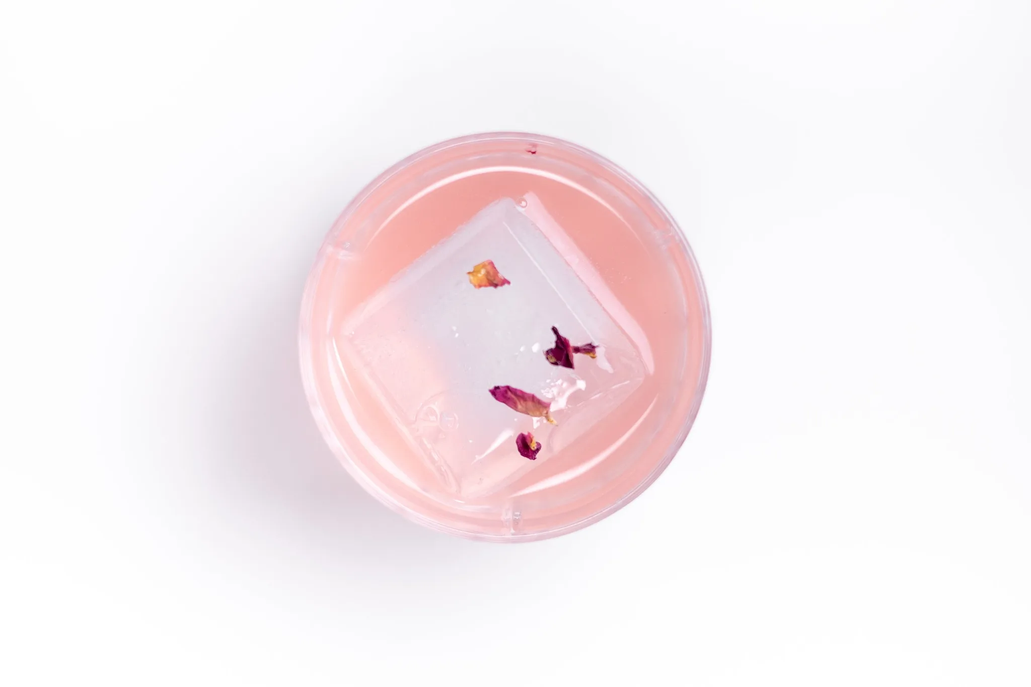 A pink drink with rose petal ice in a clear glass.