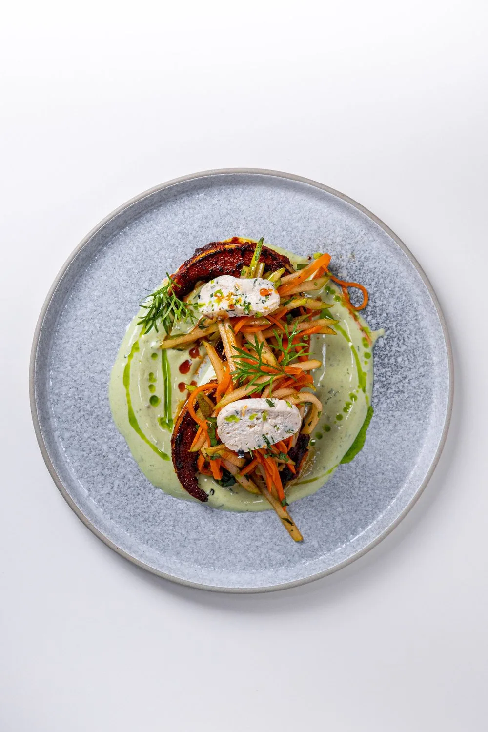 A beautifully presented chicken dish with vegetables and green sauce.