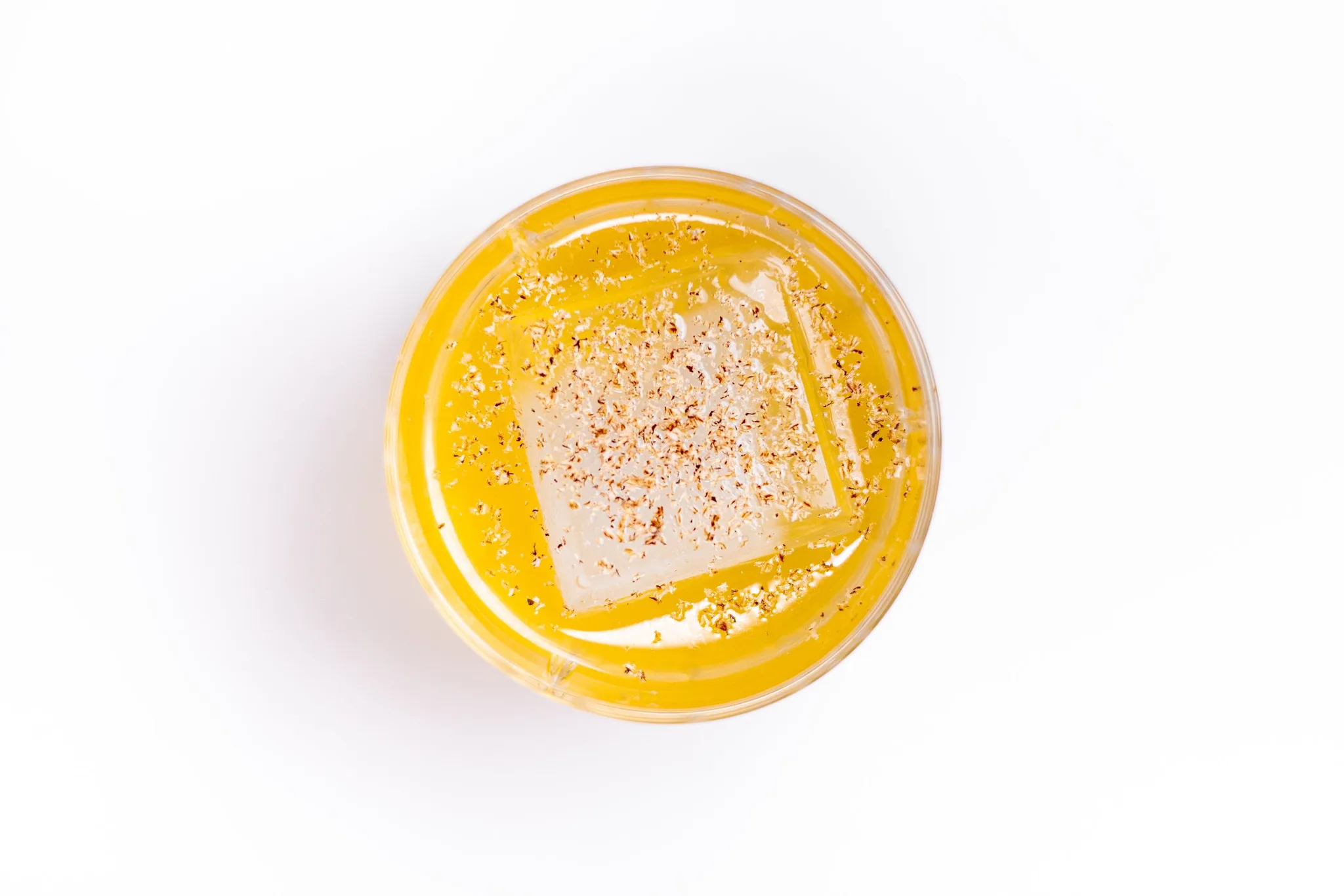 A drink with spices and an ice cube in a glass.