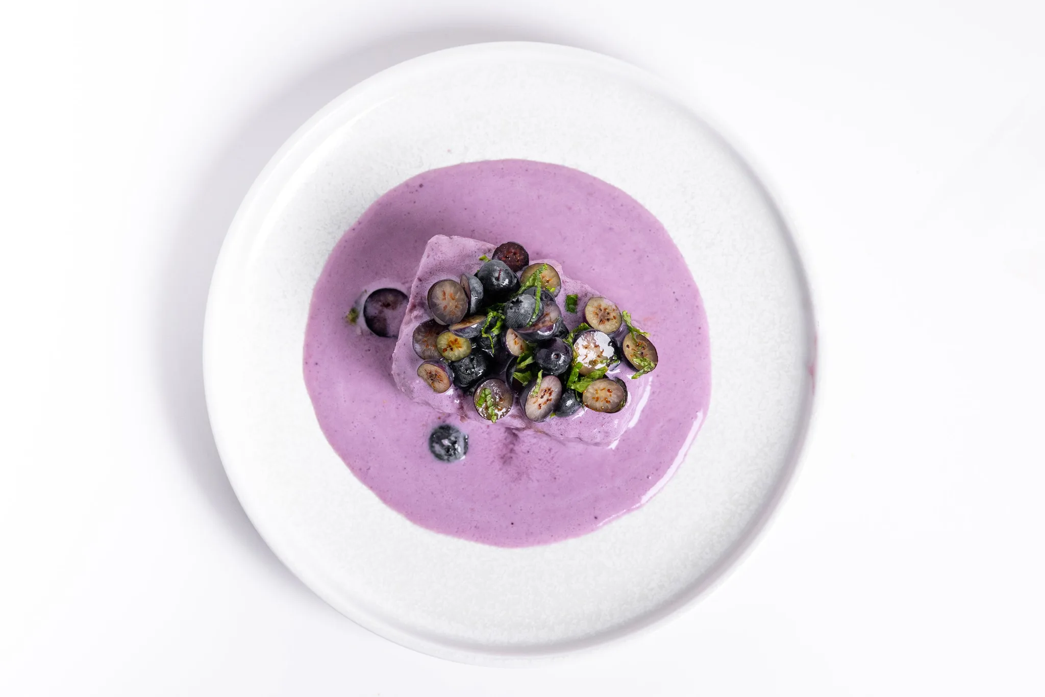 A dessert with lavender sauce and blueberries on a plate.