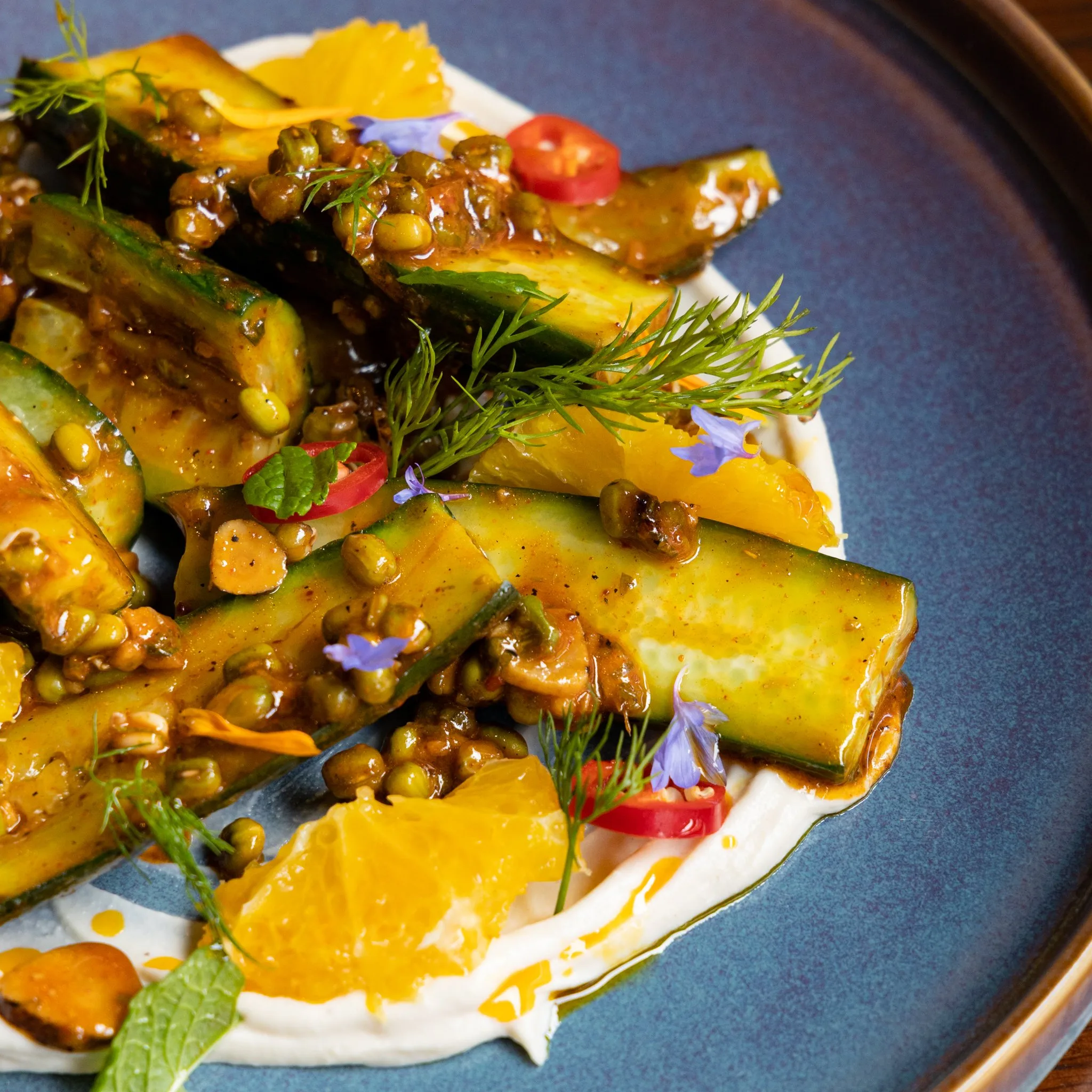 A plate of cucumber salad with sauce and orange segments.