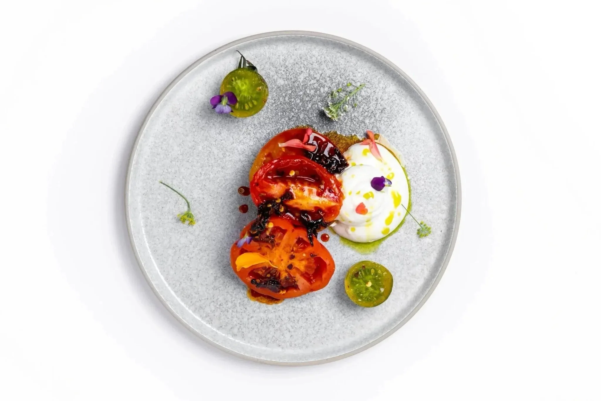 A plate of grilled tomatoes and yogurt garnished with flowers.