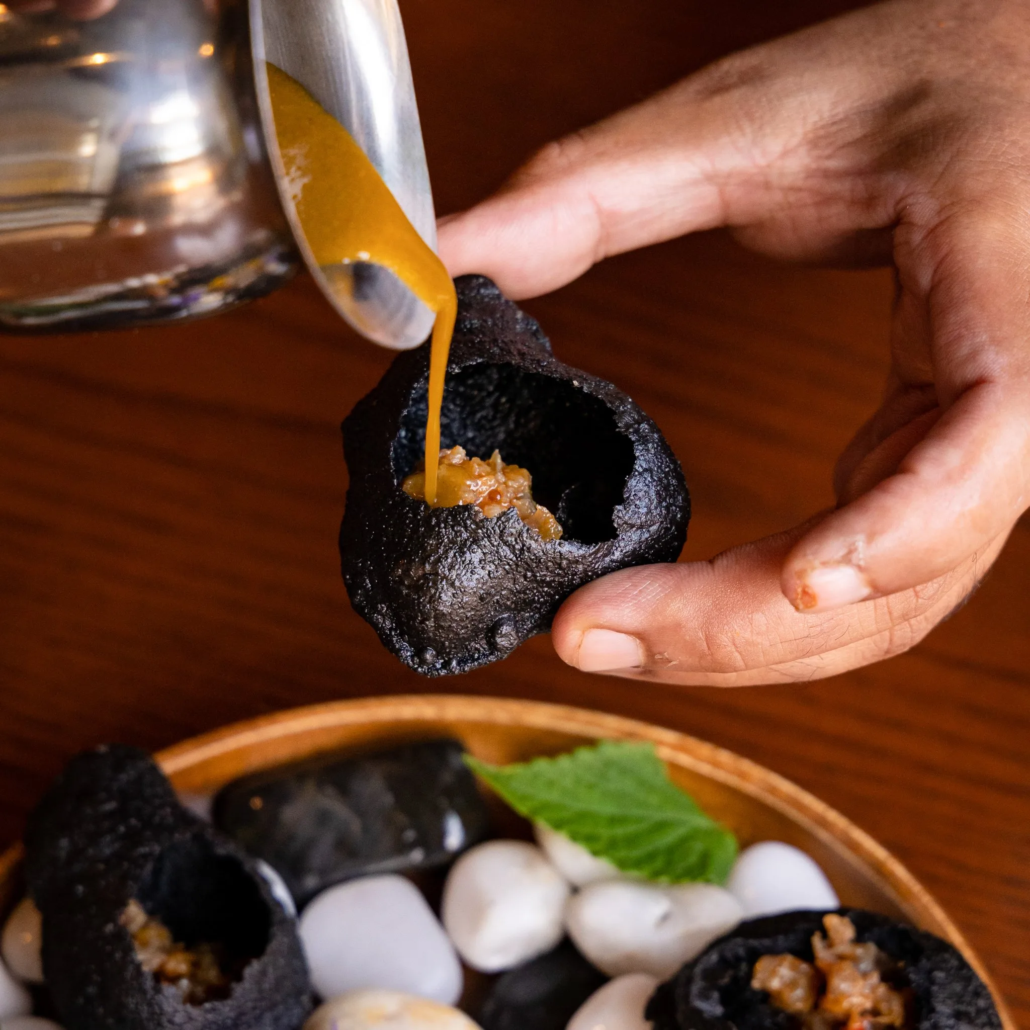 A hand pouring sauce into a crispy black shell.