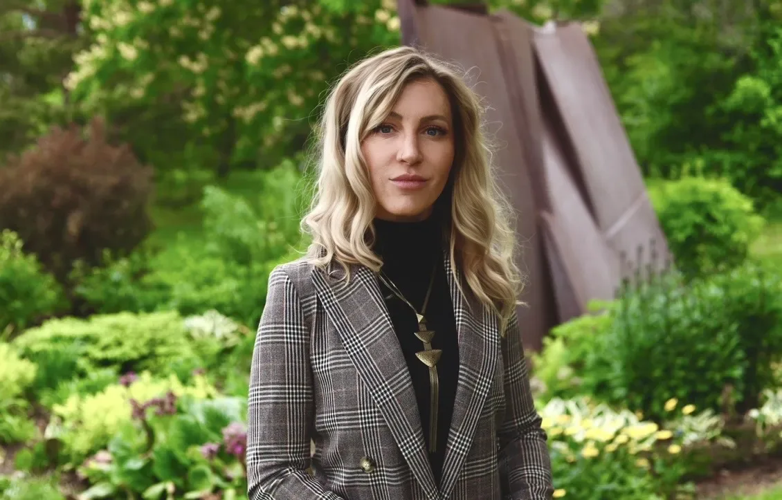 A woman in a patterned blazer stands in a garden.