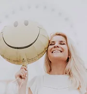 A woman smiling while holding a smiley face balloon.