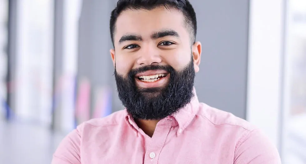 A smiling man with a beard in a pink shirt.