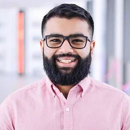 A man with glasses and a beard smiling in a bright space.