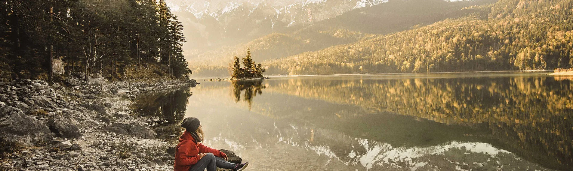 A woman in a red jacket relaxing by a lake.