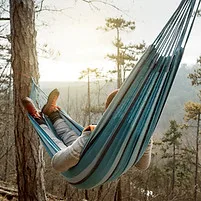 Person relaxing in a hammock in a forest setting.